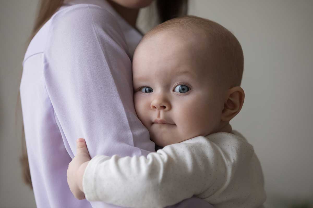Baby cuddling with person in lavender shirt.